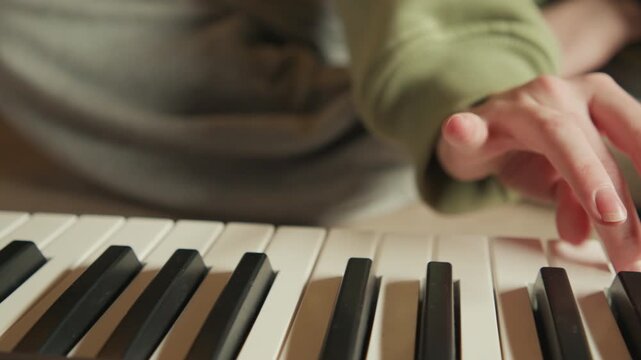 Close view of child s hand in green sleeve pressing white key on electronic keyboard, with clear fingertip contact and downward motion, while soft indoor light and blurred background keep focus on