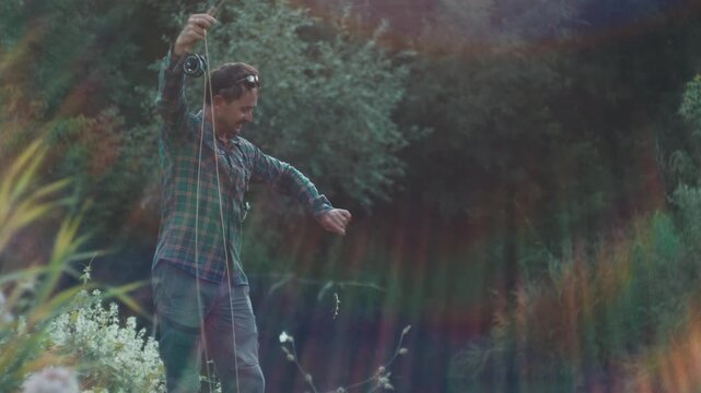 Young adult fisherman fly fishing on the small shallow river and catches the fish
