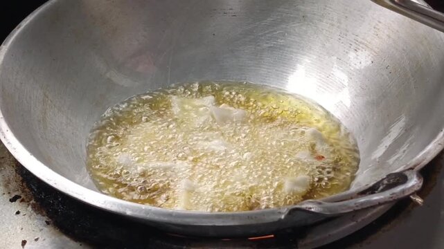 Indonesian pempek being deep fried in hot cooking oil inside a traditional metal wok, showing bubbling oil and crispy fish cake preparation in a home kitchen.