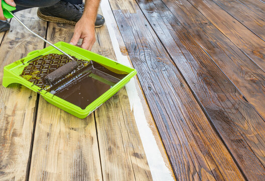 Close-up of hand rolling dark wood stain on deck