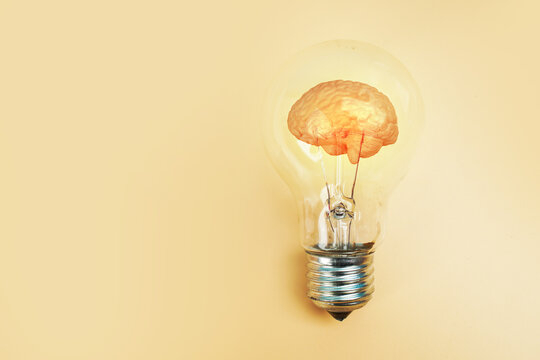 Human brain model glowing inside a light bulb on yellow background, representing creative thinking, intelligence, innovation, inspiration, ideas and brain power.