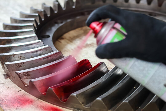 Spraying red dye penetrant onto a large industrial gear for inspection.
