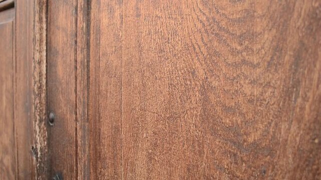 Someone is knocking on a rustic-style brown wooden door that features a natural grain pattern and surface details giving it an aged appearance.