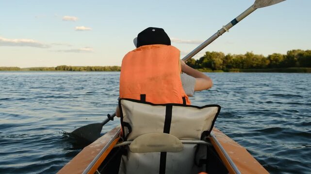 Boy in life jacket kayaking on calm river water during sunny summer day, outdoor active lifestyle and water sport concept