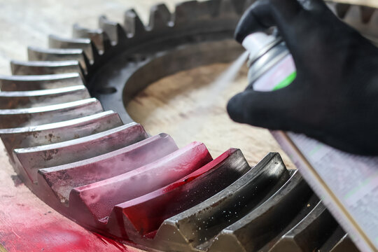 Spraying red dye penetrant or developer on a large industrial gear.