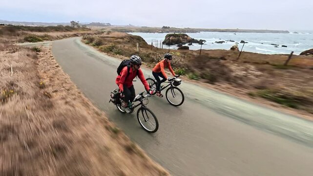 Couple rides bikes on Noyo Coastal Trail with views of cliffs and the Pacific Ocean in Fort Bragg California.