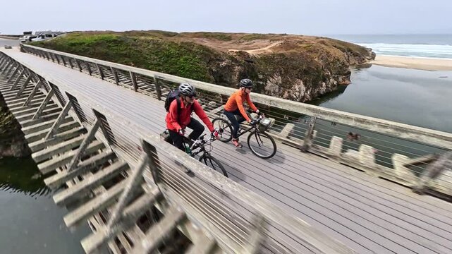 A mature man and woman bike together over Pudding Creek bridge on the coastal trail in Fort Bragg near Mendocino, California.