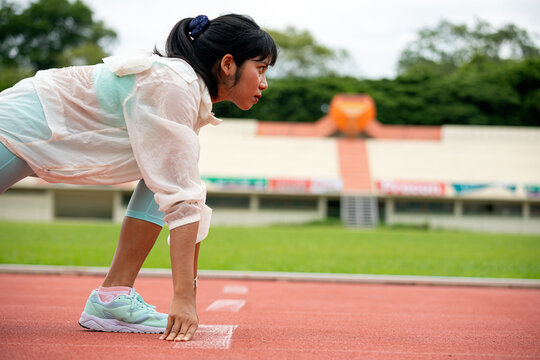 Woman athlete crouching at running track starting line, focused on sprint, race, fitness, training, competition, speed, endurance and outdoor sports performance