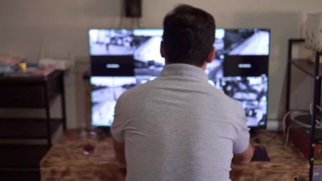 Security guard from behind reviewing CCTV camera footage on twin monitors, dark room setup, surveillance monitoring and safety observation workflow concept.