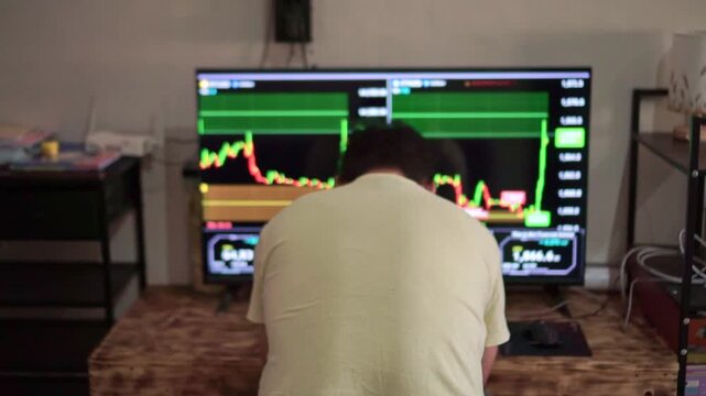 A trader bows his head in front of a live market chart on a large screen, a financial trading platform with price data, investment analysis, and stock market concepts.
