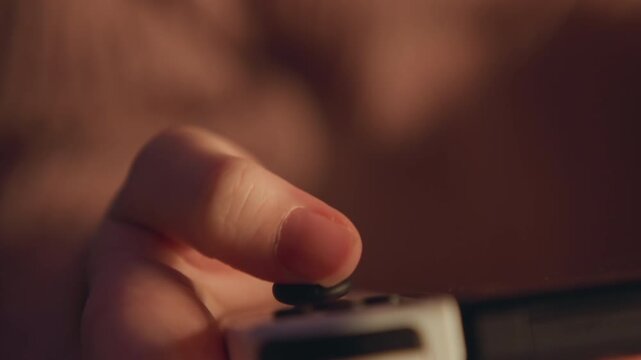 Macro oblique view of thumb pressing down on small rectangular button atop cylindrical handheld device, fingertip compression and steady grip showing tactile interaction, warm light, shallow focus