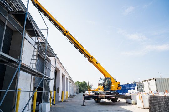 Heavy duty mobile crane truck extended high above scaffolding framework for material lifting and structural facility assembly