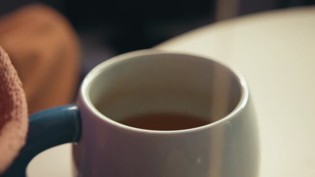 Close-up of ceramic mug filled with brewed tea after teabag removal, faint steam, gentle ripples, warm amber liquid color, and cozy tabletop setting capturing recent steeping and stirring