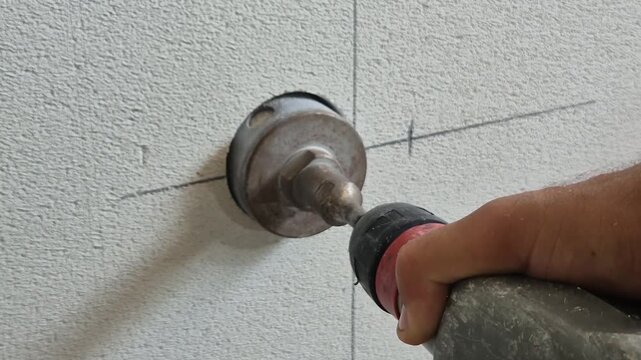 Close-up rear-side view of drilling a marked aerated concrete wall with a core drill for electrical installation.