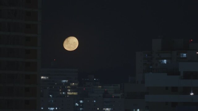 Moon rises in the sky with buildings of a city on the foreground