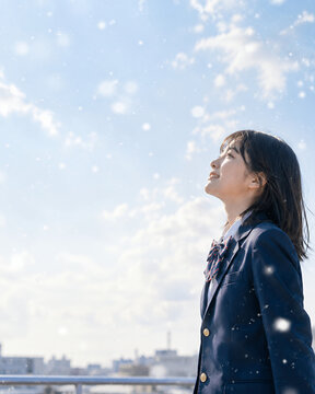 雪が舞う冬空を見上げる女子高校生　受験・進路・未来をイメージした教育素材