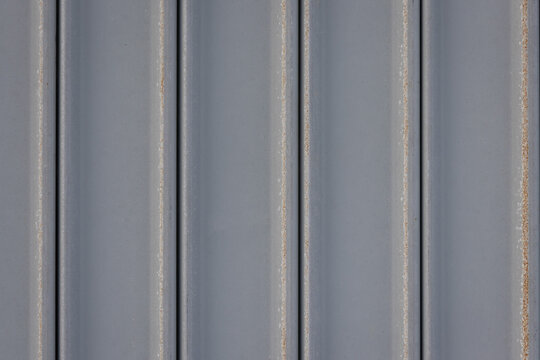 close-up, full-frame shot of a gray corrugated metal sheet with a row of rusty bolts.