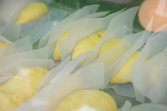 Fresh durian fruits wrapped in white paper, displayed in a market or store setting with a warm light, highlighting the distinctive yellow color and spiky texture of the fruit.