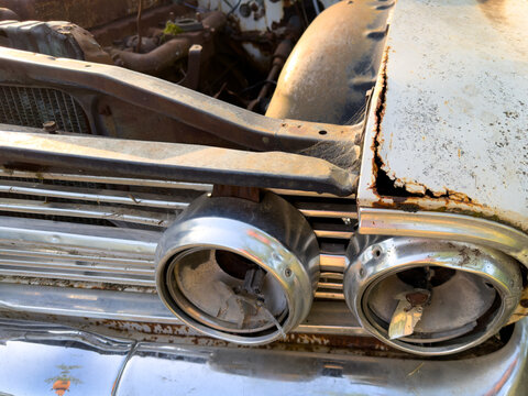Broken headlights on a dilapidated old car showing the rusty motor in the background
