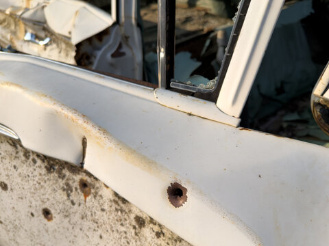 Bullet holes in dilapidated old white car with broken windows
