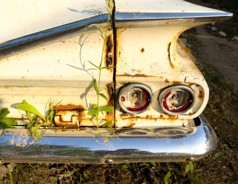 Broken taillights on an old dilapidated old rusty white car with shinny chrome bumper
