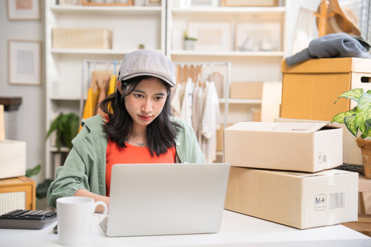 Young female online seller sitting at a desk, typing on a laptop with cardboard shipping boxes and .