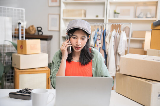 Small business owner sitting at her home office desk, making a phone call while looking at product details on her laptop.