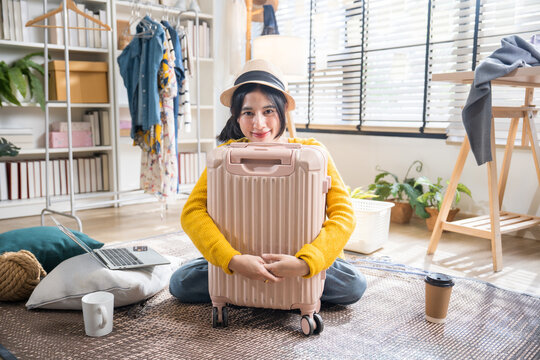 Portrait of a joyful young woman sitting on the floor and embracing her suitcase, excited for her upcoming travel vacation.