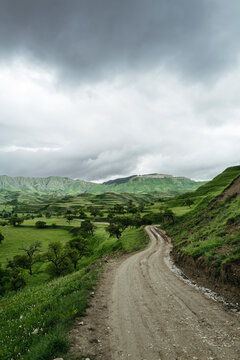 Winding Dirt Path Through Lush Green Hills Under Moody Clouds