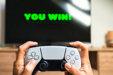 Video game controller in female hands in front of TV screen displaying You Win. © Igor Barilo