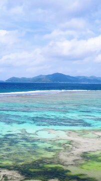 Vertical ascending aerial view of Anse Source d'Argent in Seychelles revealing turquoise water, coral reef, granite rocks and spectacular tropical coastal scenery.