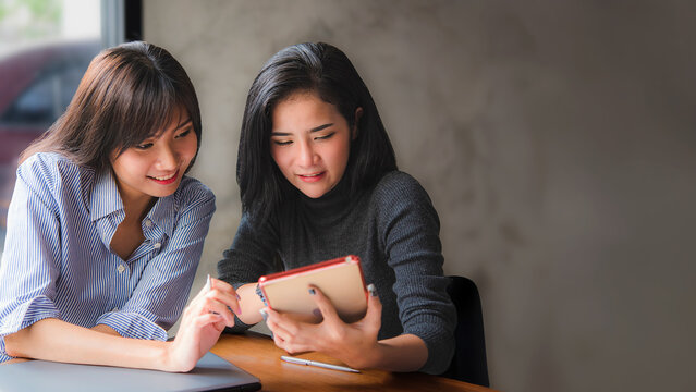 Two Young Asian woman learning and reading a book together at coffee shop or cafe in the morning, vintage tone 