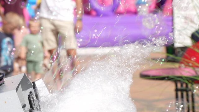 Automatic bubble machine blower blowing dense soap foam and iridescence soap bubbles outdoors during a children festival