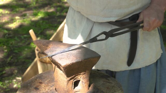 A blacksmith is crafting a metal item by hammering a hot metal workpiece on an anvil. 4k video shot.