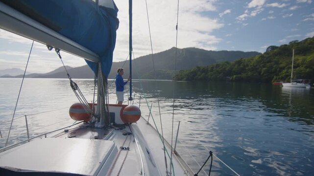 Young man enjoys the morning time on the sailing boat anchored in the calm bay