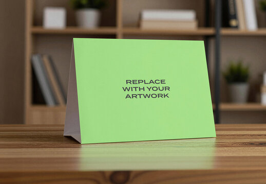 Table tent sign mockup displayed on a wooden surface in an office environment with bookshelf and indoor plant, realistic stationery branding presentation template