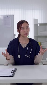 Young Asian female doctor explaining medical information during telehealth video consultation in bright clinic office