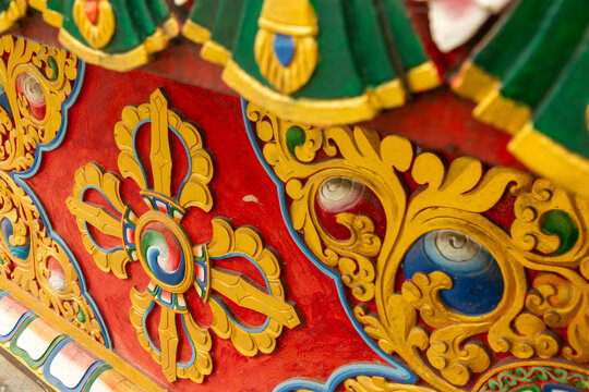 View of intricate, hand-painted Buddhist wood carvings featuring a golden vajra symbol and vibrant floral patterns on a temple structure in Pokhara, Gandaki Province, Nepal.