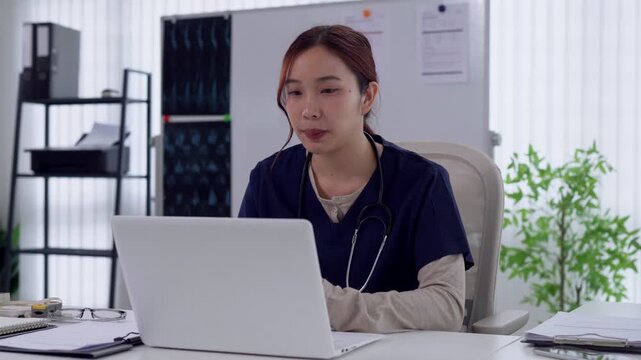 Young Asian female doctor conducting telemedicine video consultation on laptop in modern medical office