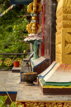 View of a smoking incense burner on a stone ledge in front of an ornate temple with gold carvings and prayer wheels in Pokhara, Gandaki Province, Nepal.