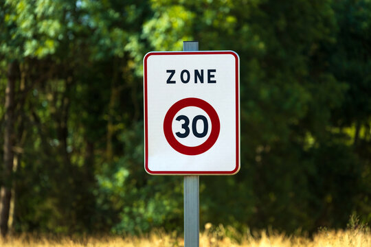 Panneau de signalisation indiquant une zone limit&eacute;e &agrave; 30 km/h dans un quartier r&eacute;sidentiel bord&eacute; d&rsquo;arbres, en &eacute;t&eacute;. Ambiance calme et verdoyante.