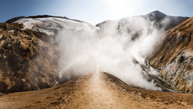 View of Kerlingarfjoll mountain range with geothermal steam rising from the rocky terrain and snow-capped peaks in Hrunamannahreppur, Iceland.