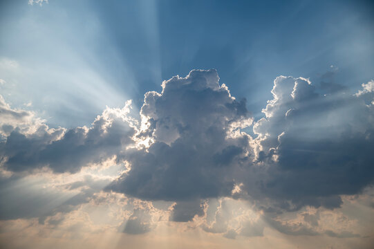 Dramatic Sun Rays Bursting Behind Dark Clouds in Blue Sky.

