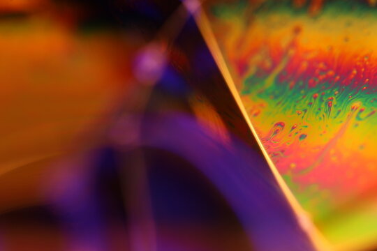 Multi-color liquid film plane with rainbow iridescence and specular edge line. A low-key macro perspective capturing an iridescent liquid film facet glowing with vibrant spectrum colors 