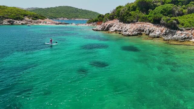 Woman on sup board in Ksamil near Twin Islands, Ionian Sea, Saranda, Albania. Stand up paddle board woman paddle boarding. Aerial panoramic drone view from above, top view from drone. Mediterranean se