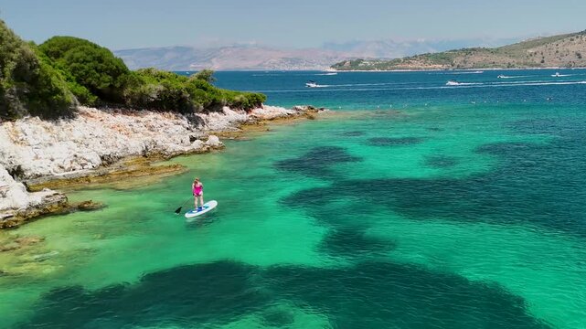Woman on sup board in Ksamil near Twin Islands, Ionian Sea, Saranda, Albania. Stand up paddle board woman paddle boarding. Aerial panoramic drone view from above, top view from drone. Mediterranean se