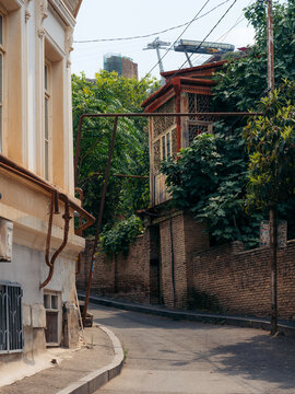 View of Old Tbilisi with traditional brick walls, wooden balconies, and lush greenery along a narrow street, with the aerial tramway visible in the background in Tbilisi, Tbilisi, Georgia.