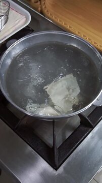 Chef wearing white gloves boiling fresh dough sheets for beshbarmak in a metal pot with wire skimmer