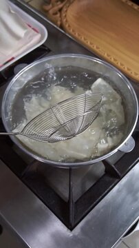 Chef wearing white gloves boiling fresh dough sheets for beshbarmak in a metal pot with wire skimmer