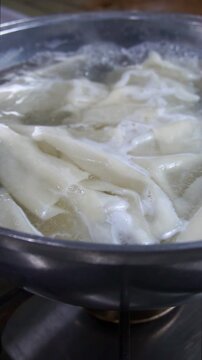 Close-up of fresh dough sheets boiling in hot water inside a metal pot for traditional beshbarmak
